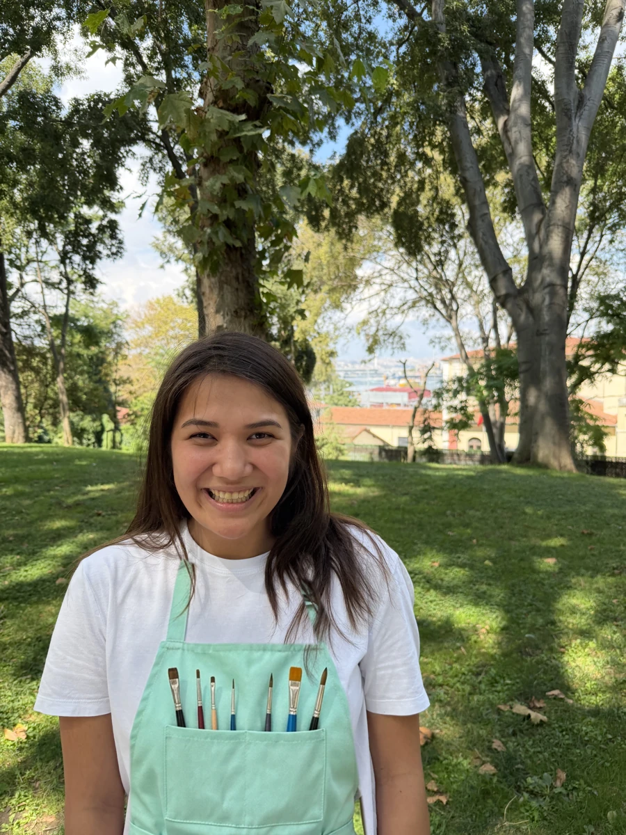 Victoria smiling outdoors, wearing a mint face-painting apron with brushes
